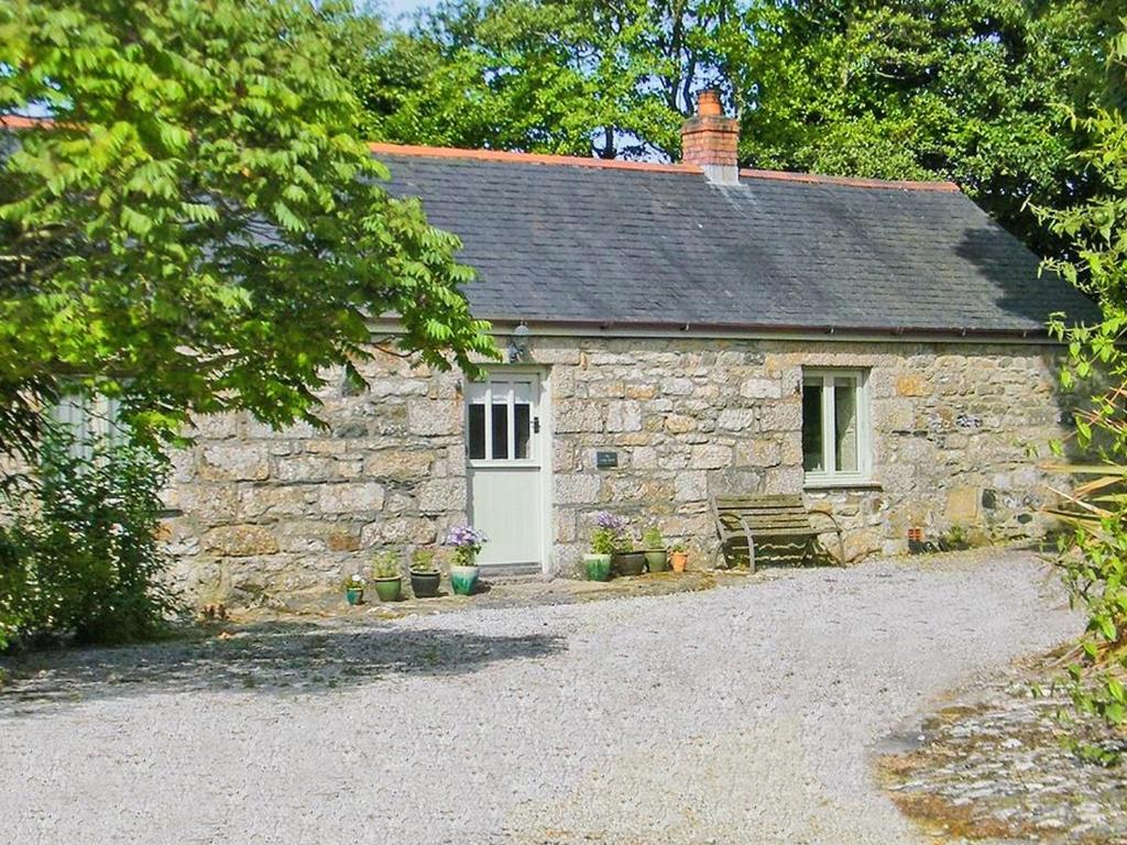 a stone cottage with a white door and a bench at The Long Barn in Crowan