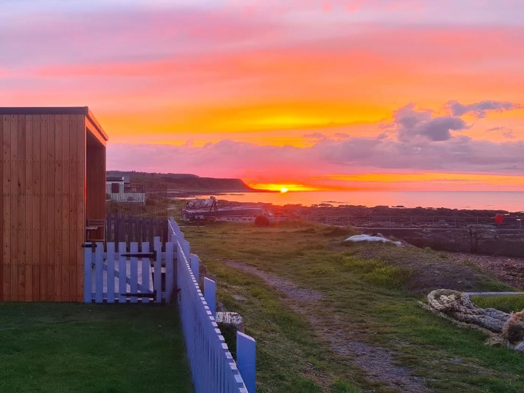 a sunset over the ocean with a white fence at Sunrise Summerhouse in Balintore