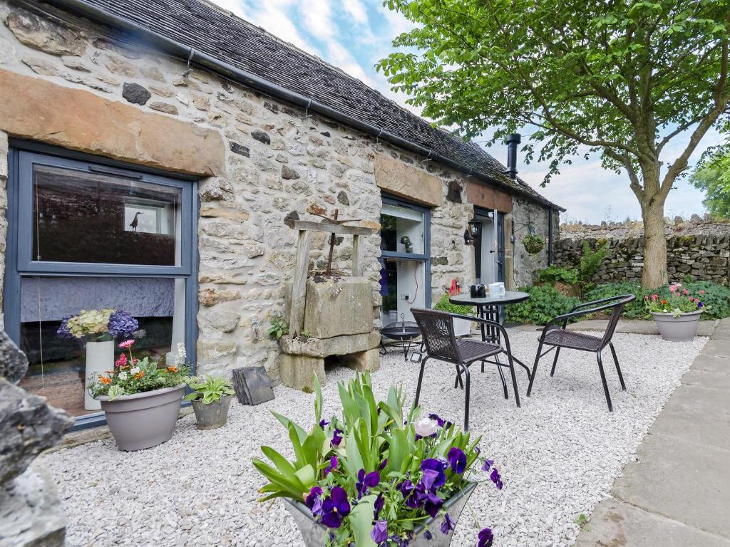a stone cottage with chairs and a table and flowers at Baileys Barn in Bonsall