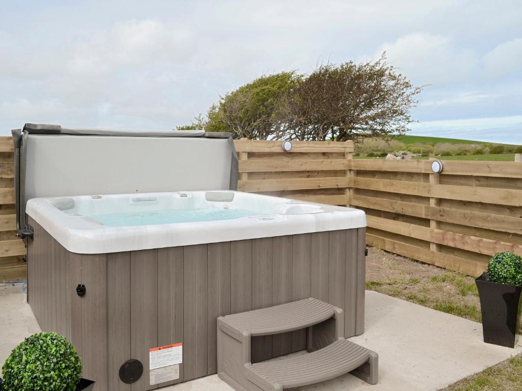 a hot tub in a backyard with a wooden fence at Llofft Storws in Valley