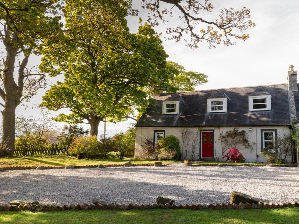 uma casa com uma porta vermelha e uma entrada de cascalho em Garden Cottage em Tain