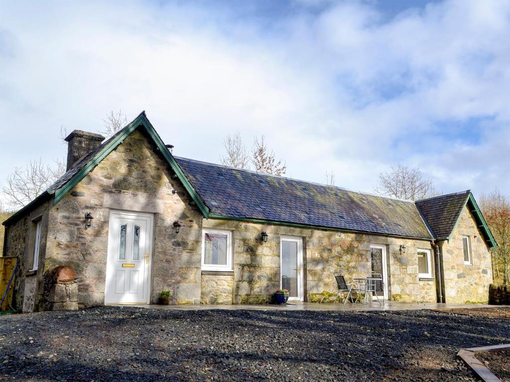 a stone house with a white door at The Old Inverchroskie Kennels in Enochdhu