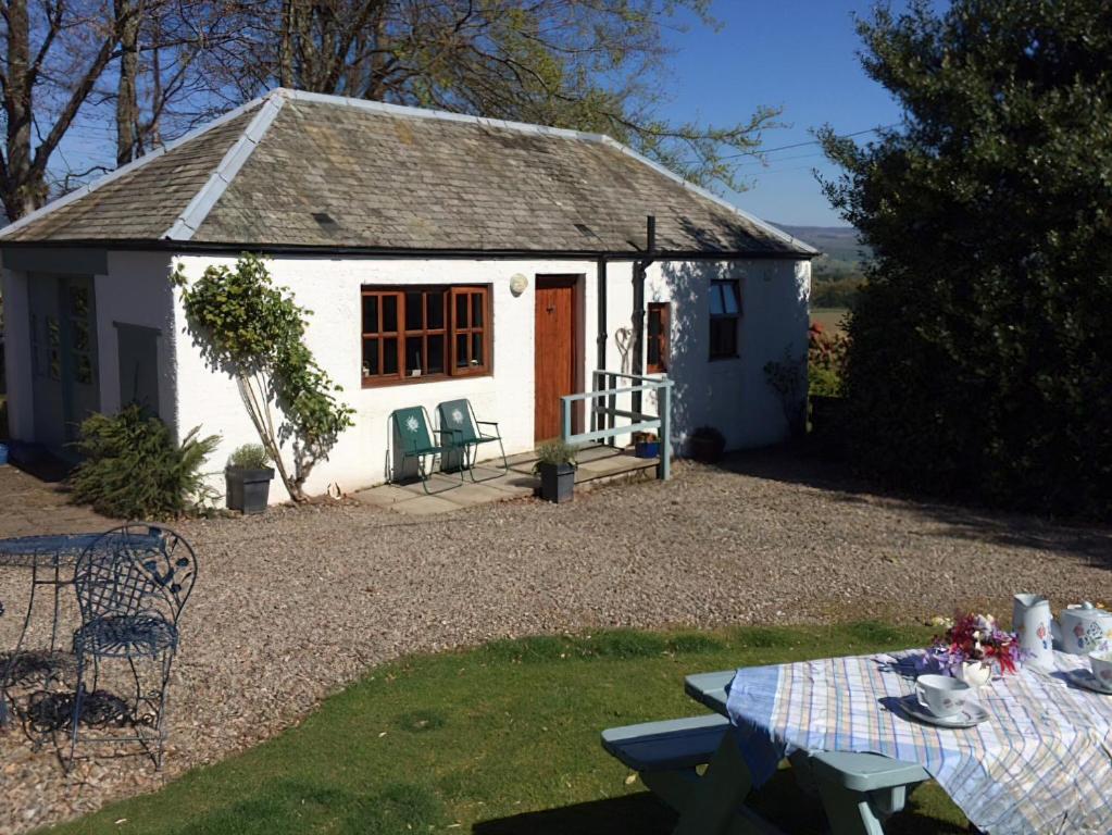 una pequeña casa de campo blanca con una mesa delante en The Wee House en Muthill