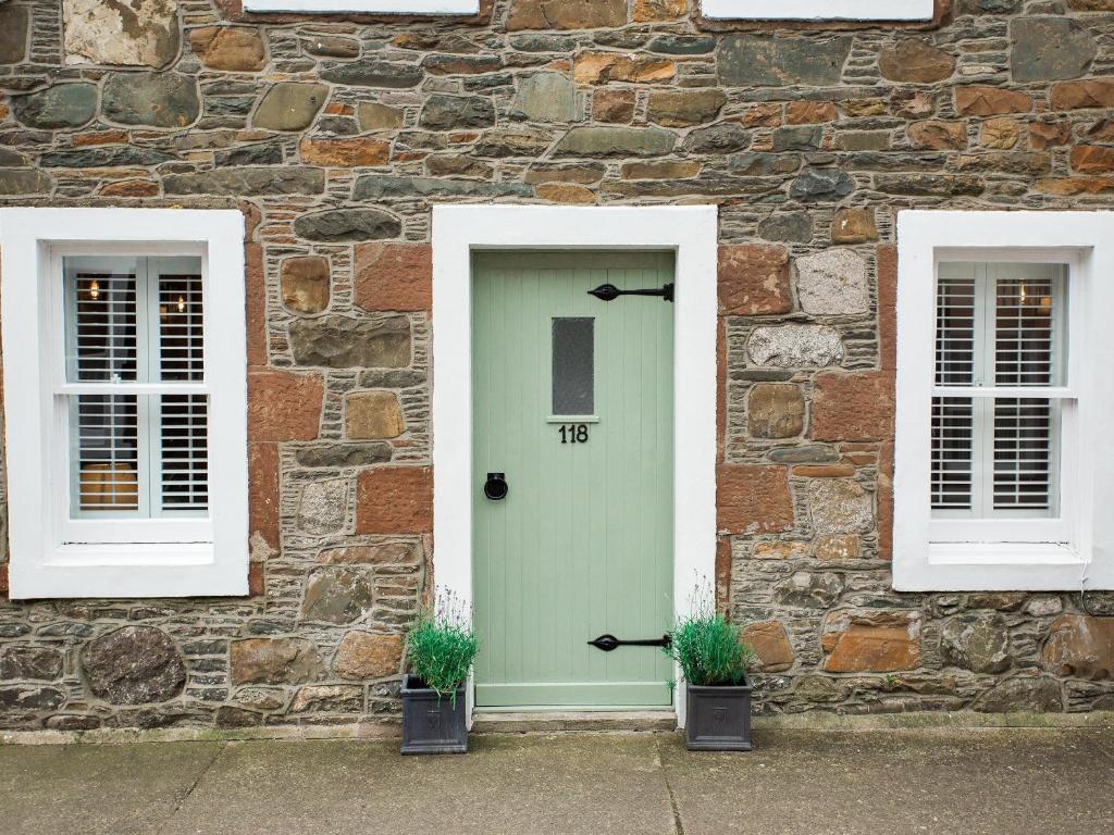 a stone building with a green door and two windows at High Street in Kirkcudbright
