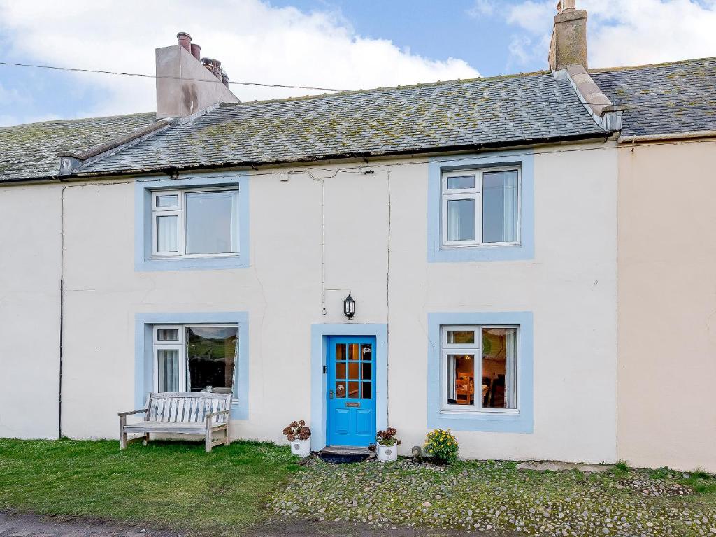 a white house with a blue door and a bench at Curlew Cottage in Mawbray