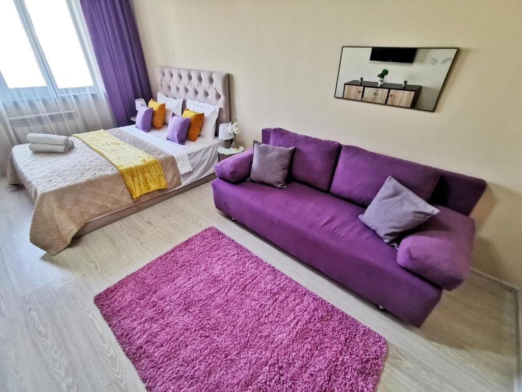 ein Wohnzimmer mit einem lila Sofa und einem Bett in der Unterkunft Appartments " Zhetysu-4" in Almaty