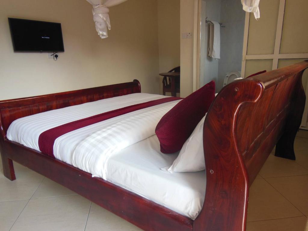een houten bed met twee rode kussens erop bij Psalms Motel in Entebbe