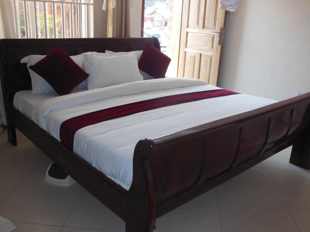 a bed with a wooden frame with pillows on it at Psalms Motel in Entebbe