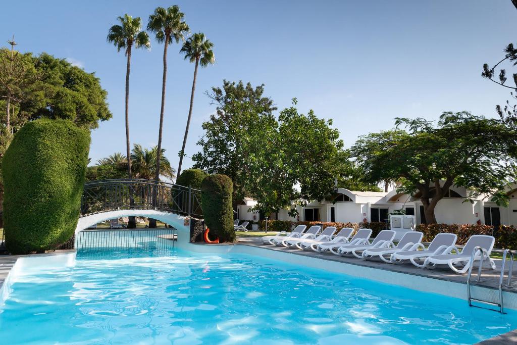 una piscina con sillas, un puente y palmeras en Bungalows Cordial Biarritz, en Playa del Inglés