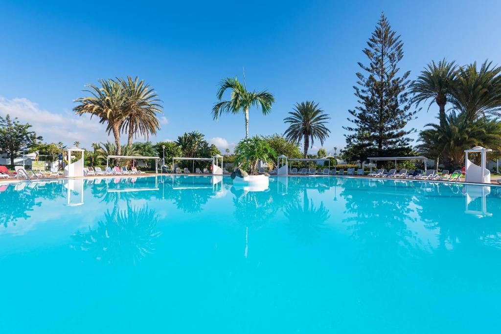 una gran piscina con palmeras en el fondo en Bungalows Cordial Sandy Golf, en Maspalomas