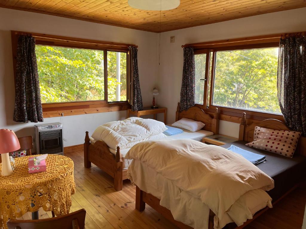 um quarto com 2 camas, uma mesa e 2 janelas em Ohisama House em Rusutsu