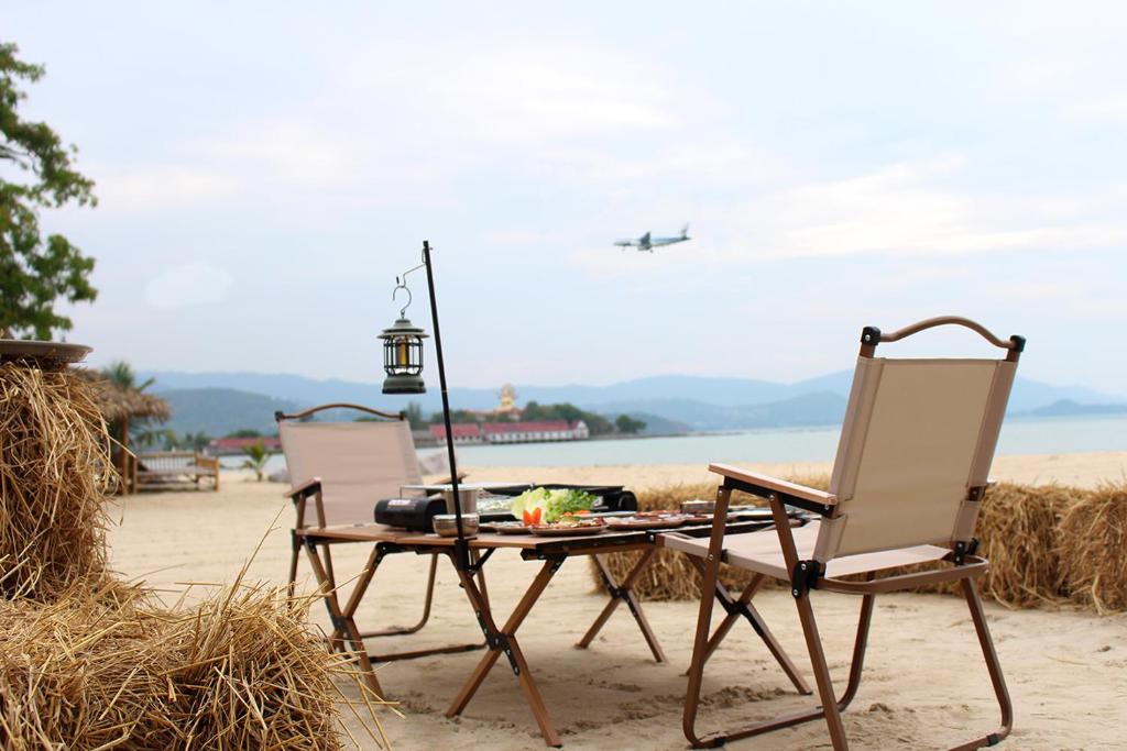 two chairs and a table and an airplane in the sky at Deva Beach Resort Samui in Choeng Mon Beach