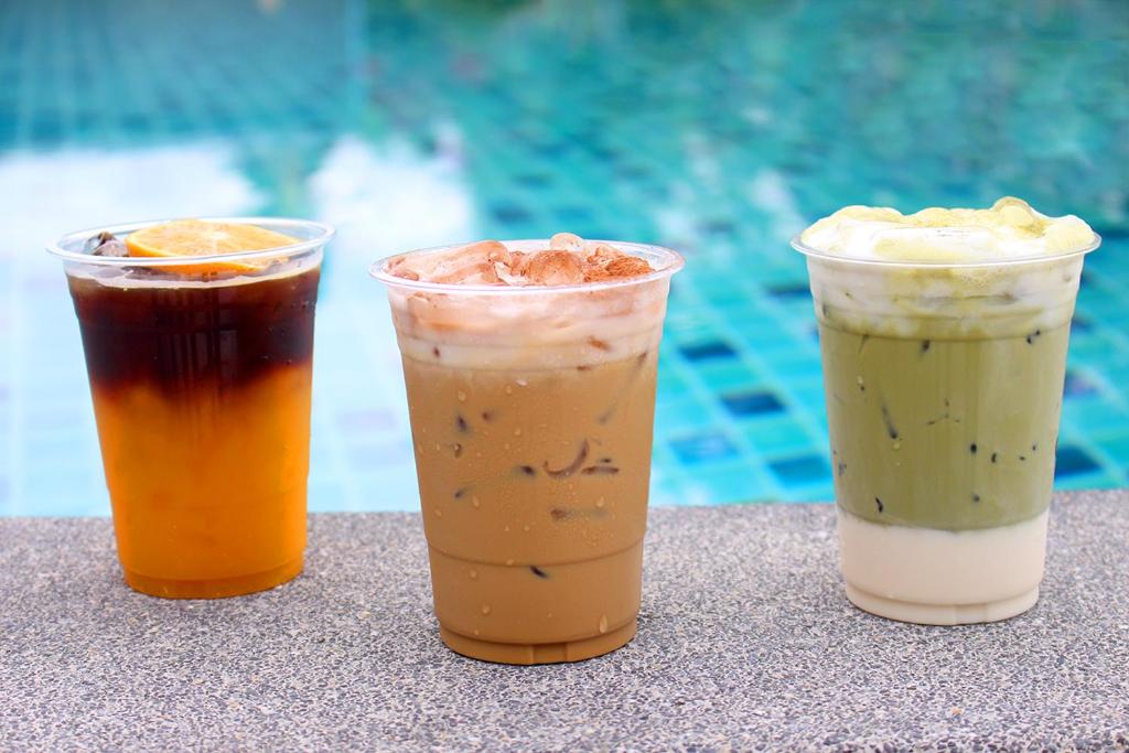 three drinks sitting on a table next to a pool at Deva Beach Resort Samui in Choeng Mon Beach