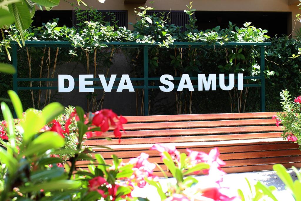 a wooden bench in front of a sign with flowers at Deva Beach Resort Samui in Choeng Mon Beach