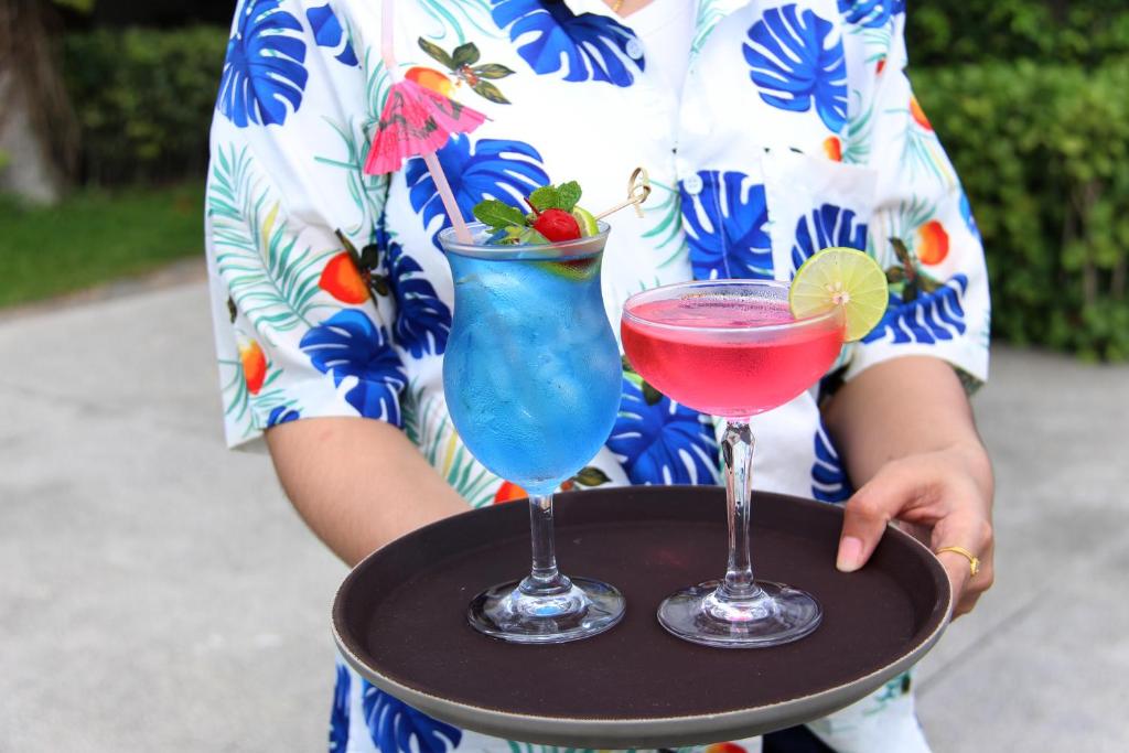 a woman holding a tray with two cocktails on it at Deva Beach Resort Samui in Choeng Mon Beach