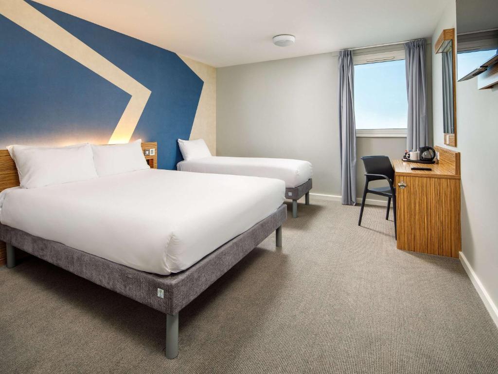 a hotel room with two beds and a desk at ibis budget London Heathrow Central in Hounslow