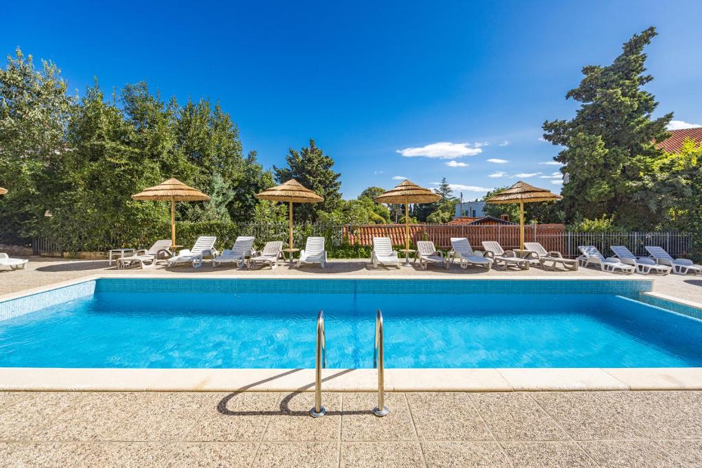 a swimming pool with chairs and umbrellas at Residence Kamenjak in Premantura
