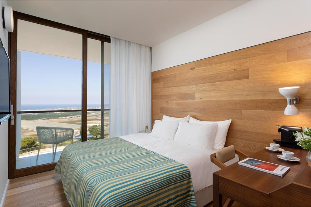 a hotel room with a bed and a desk and a window at Elma Hotel and Art Complex in Zikhron Ya'akov