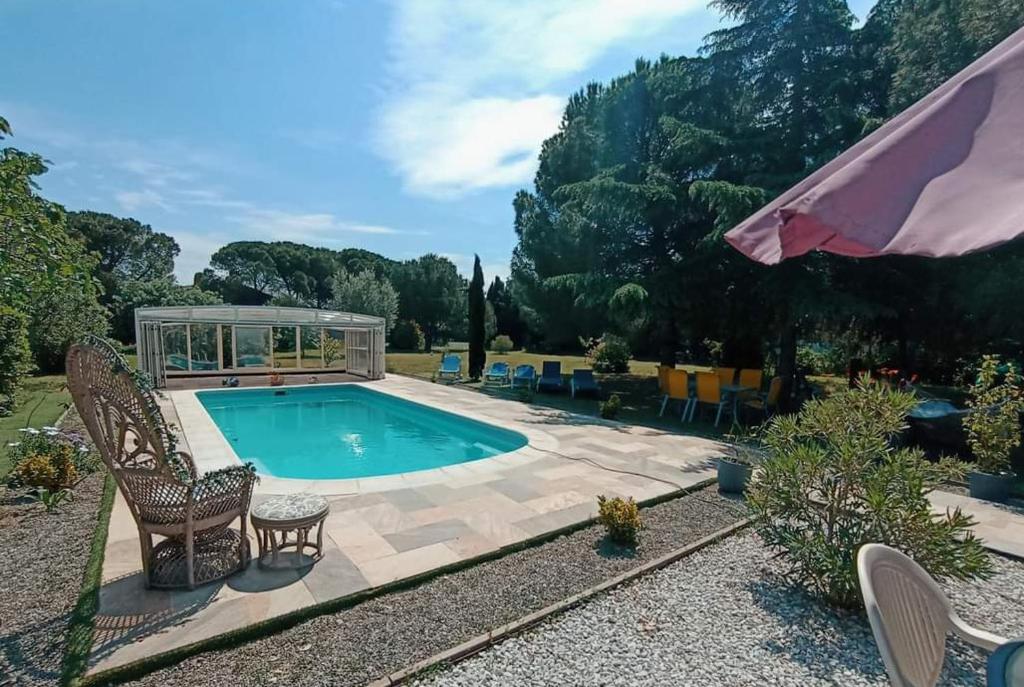 una piscina en un jardín con sillas y sombrilla en Mas des 2 paons, en Villedaigne