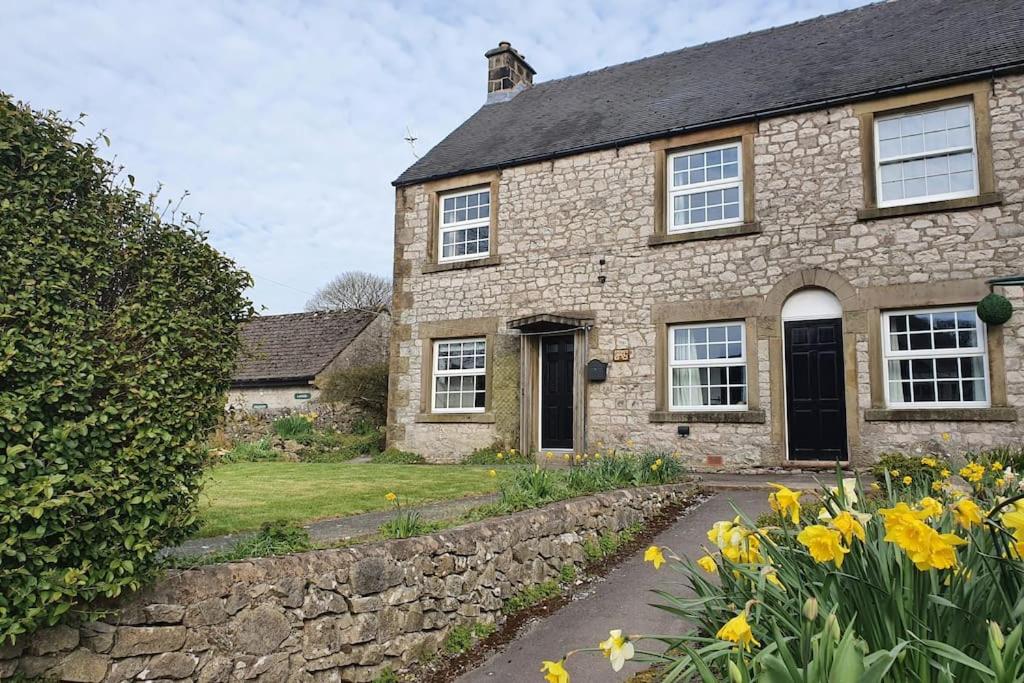 une maison en pierre avec des fleurs jaunes devant elle dans l'établissement Dove View Hartington: luxury 3 bed cottage, à Hartington