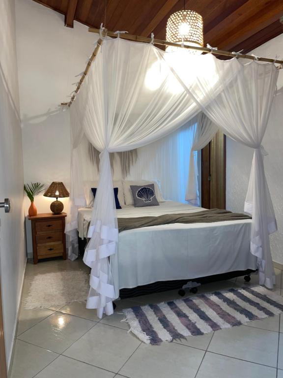 1 dormitorio con cama con dosel y cortinas blancas en Casa em Cabo Frio, en Cabo Frío