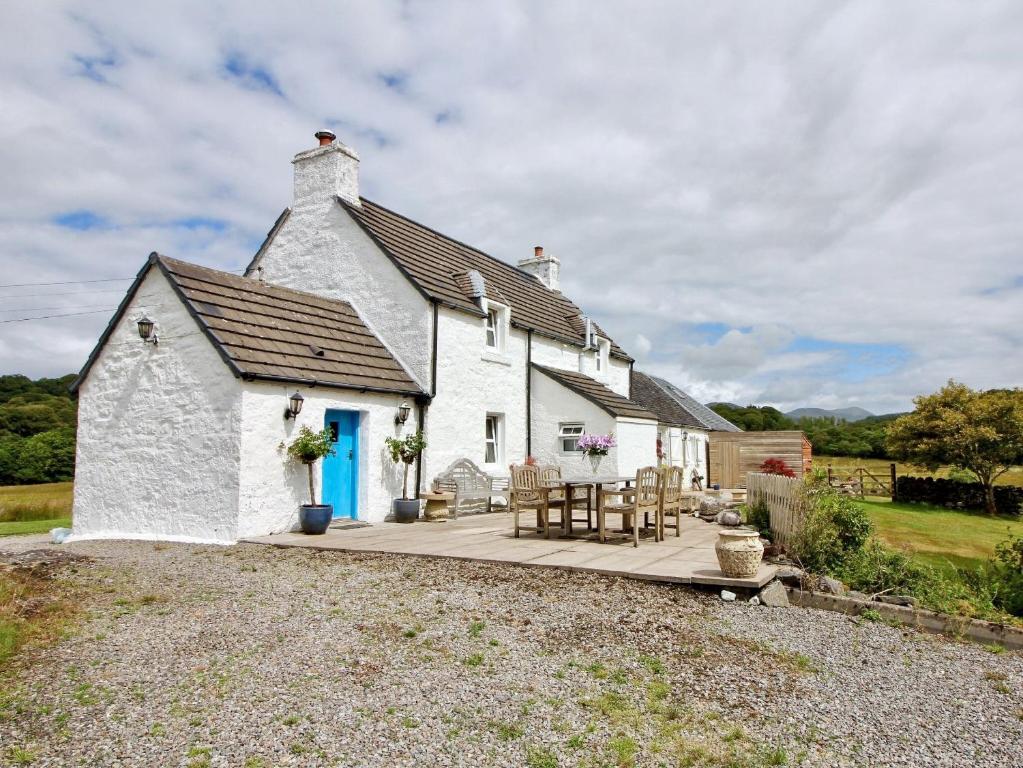 a white cottage with a blue door and a patio at Coelard Farmhouse in Appin