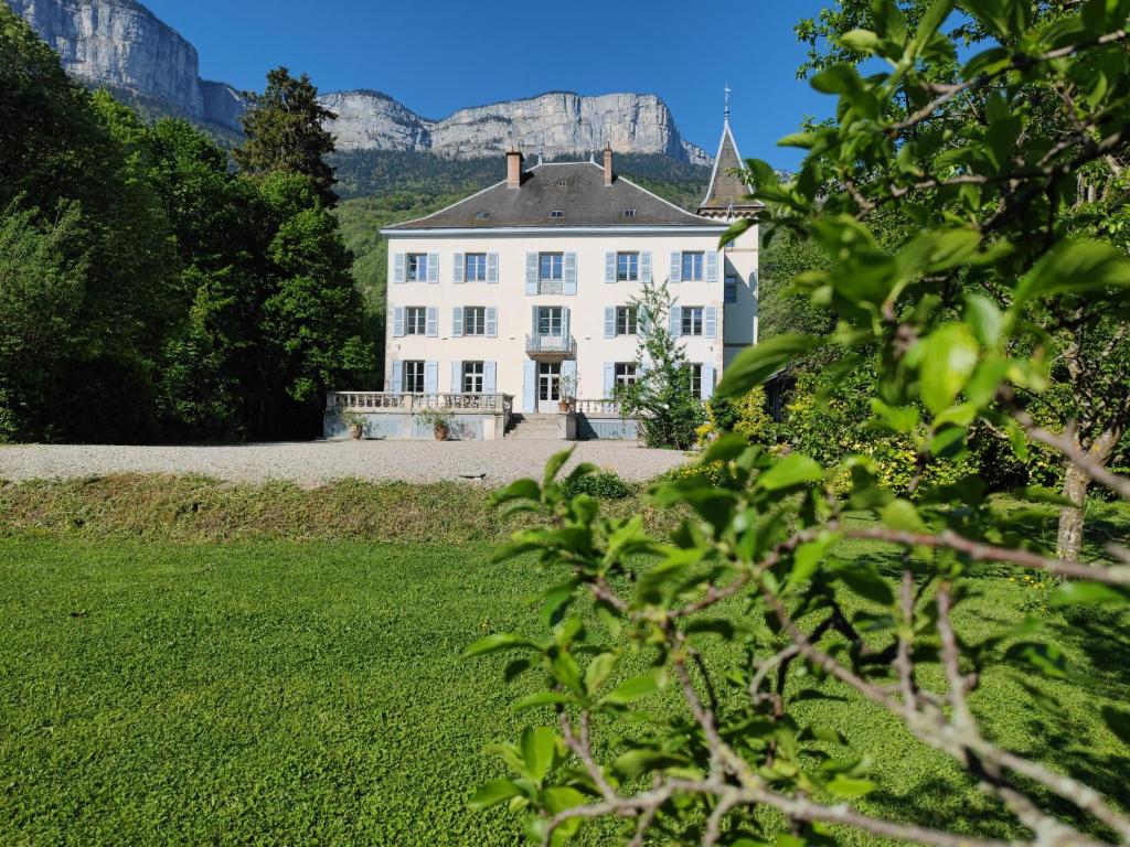 Une grande maison blanche avec une montagne en arrière-plan dans l'établissement Domaine Clairfontaine Noyarey - Suites Junior, à Noyarey