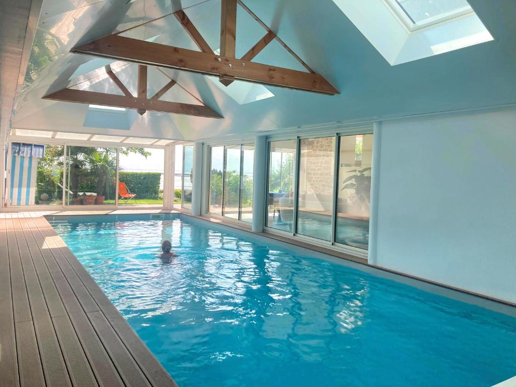 a person swimming in a large swimming pool with windows at Manava Villa vue mer et Mont Saint Michel piscine intérieure in Saint-Jean-le-Thomas