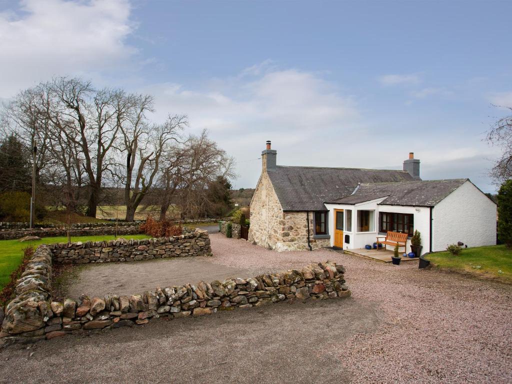 a stone house with a stone wall in front of it at Craigellachie Cottage in Croy