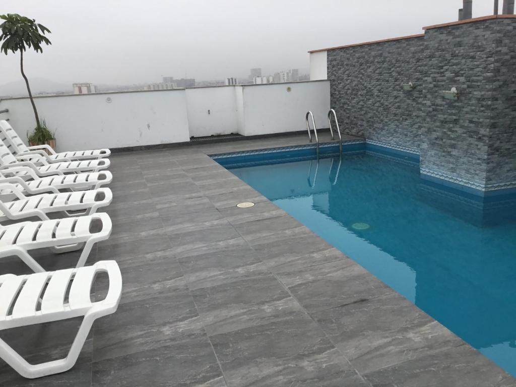 une piscine avec des chaises longues blanches sur le toit dans l'établissement Hermoso Departamento - Oficina, à Lima
