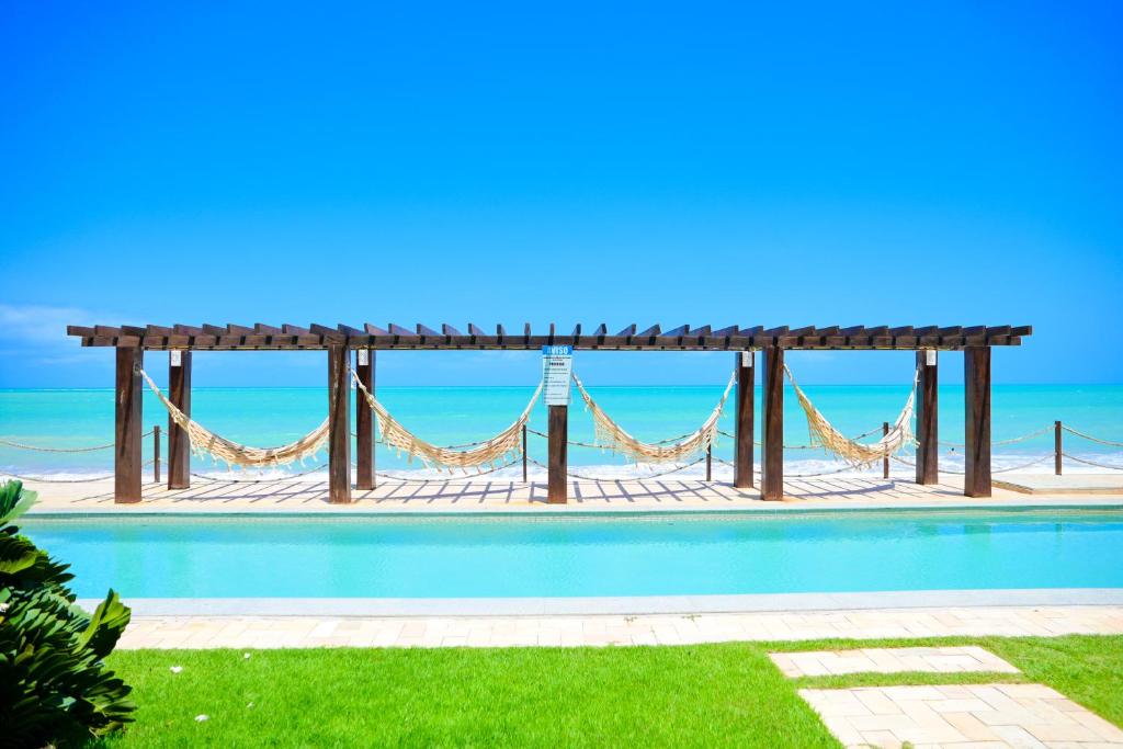 a swimming pool with a hammock and the ocean at Waterfront Apart Hotel in Maceió