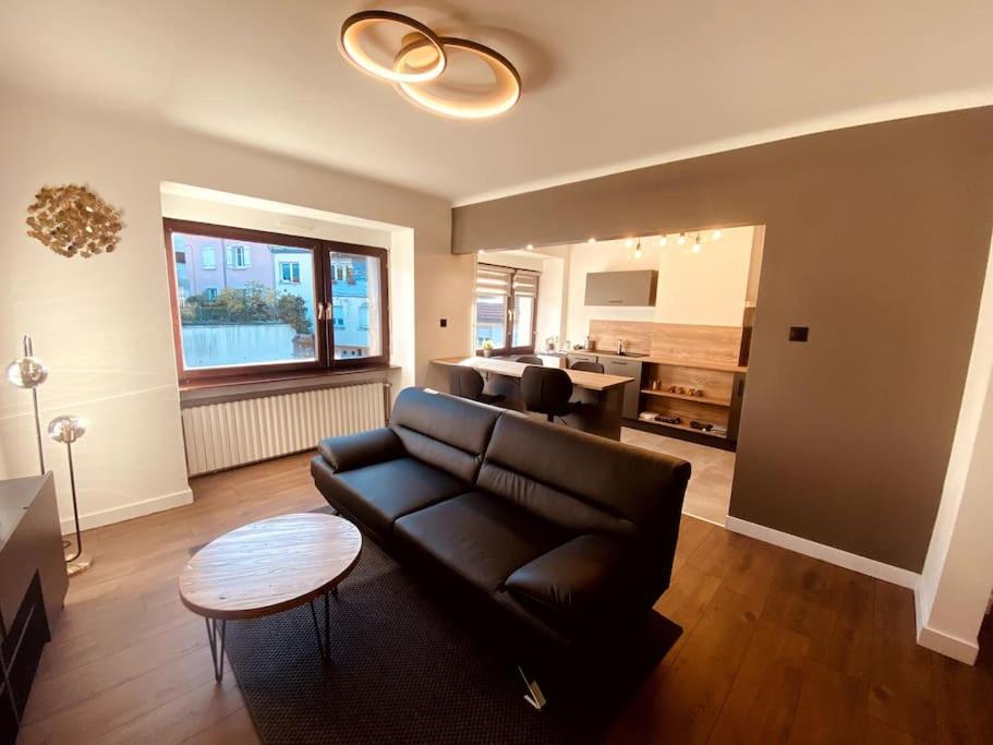 a living room with a black leather couch and a table at Appartement en centre-ville in Saint-Avold