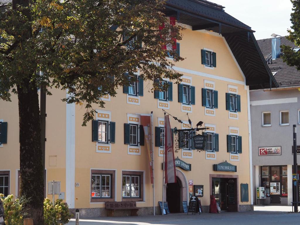 un grand bâtiment jaune avec des fenêtres noires et un arbre dans l'établissement Landgasthof Santner, à Thalgau