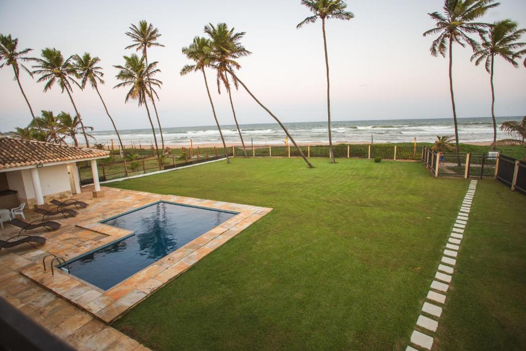einen Hinterhof mit einem Pool und einer Liegewiese mit Palmen in der Unterkunft Maravilhosa casa em Vilas do Atlantico frente ao mar in Lauro de Freitas