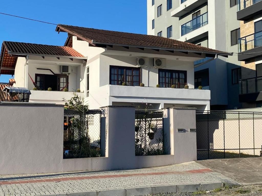uma casa branca com uma cerca em frente a um edifício em RCM Vilas - Casa confortável 1 em Joinville