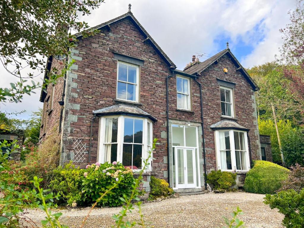 a brick house with white windows and bushes at Little Parrock, Grasmere in Grasmere