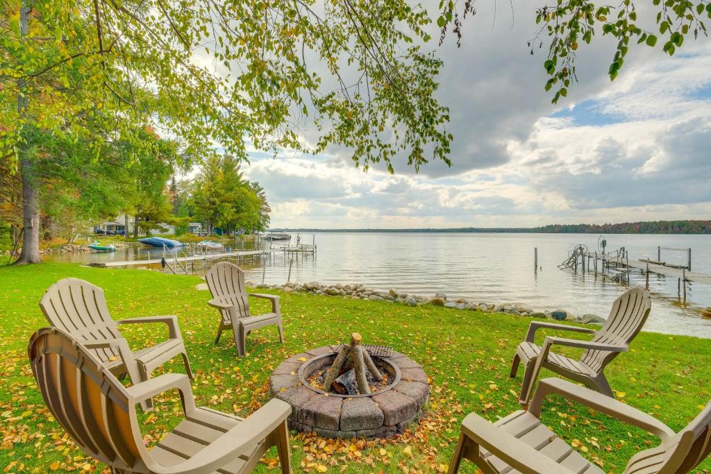 a group of chairs sitting around a fire pit by the water at Kalkaska Retreat Private Hot Tub, Dock, Fireplace in Kalkaska