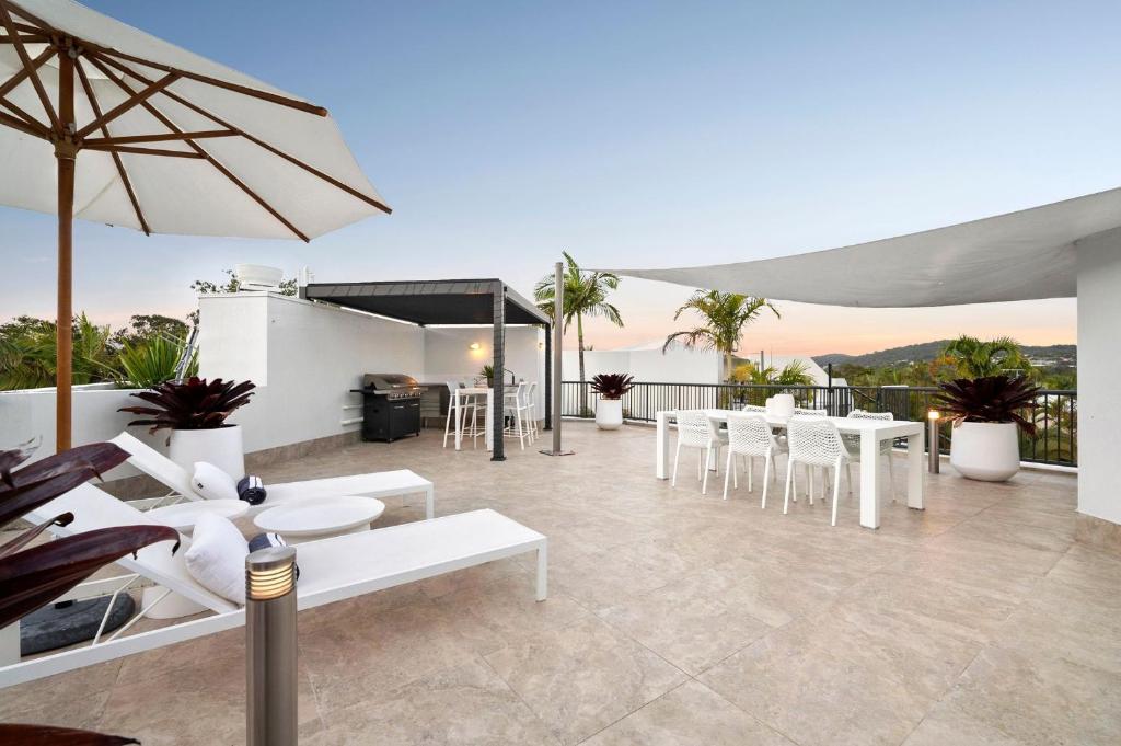 a patio with white chairs and tables and an umbrella at Penthouse with Private Roof top terrace- NOOSA in Noosa Heads
