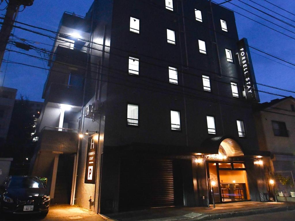 ＦＯＲＢＥＬＬ　ＳＴＡＹ　ＹＵＲＩＧＡＯＫＡ في Ikuta: مبنى أسود طويل مع نوافذ مضاءة في الليل