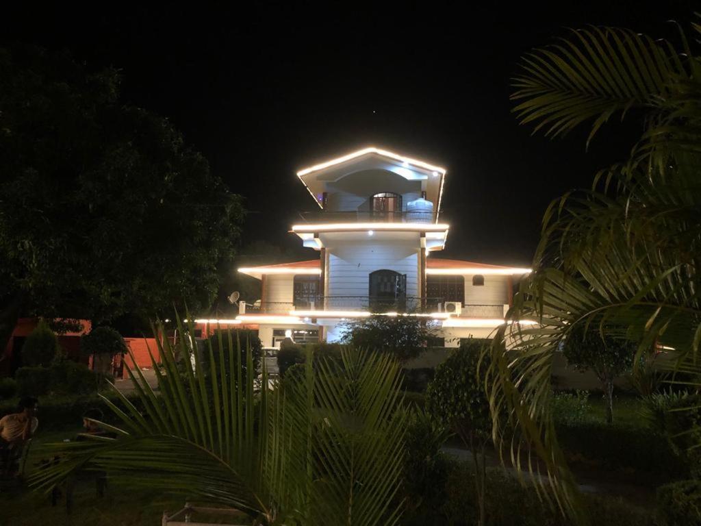 a white building with a light tower at night at Corbett Atulyam Home Stay in Rāmnagar