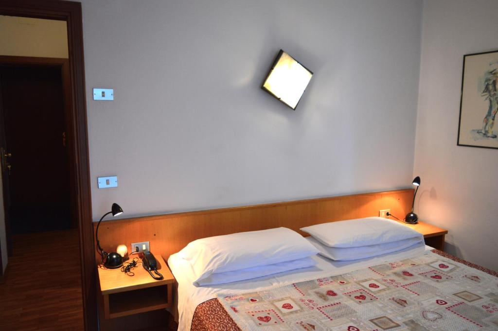 a bedroom with a bed with white sheets and a mirror at Hotel Wanda in Pinzolo