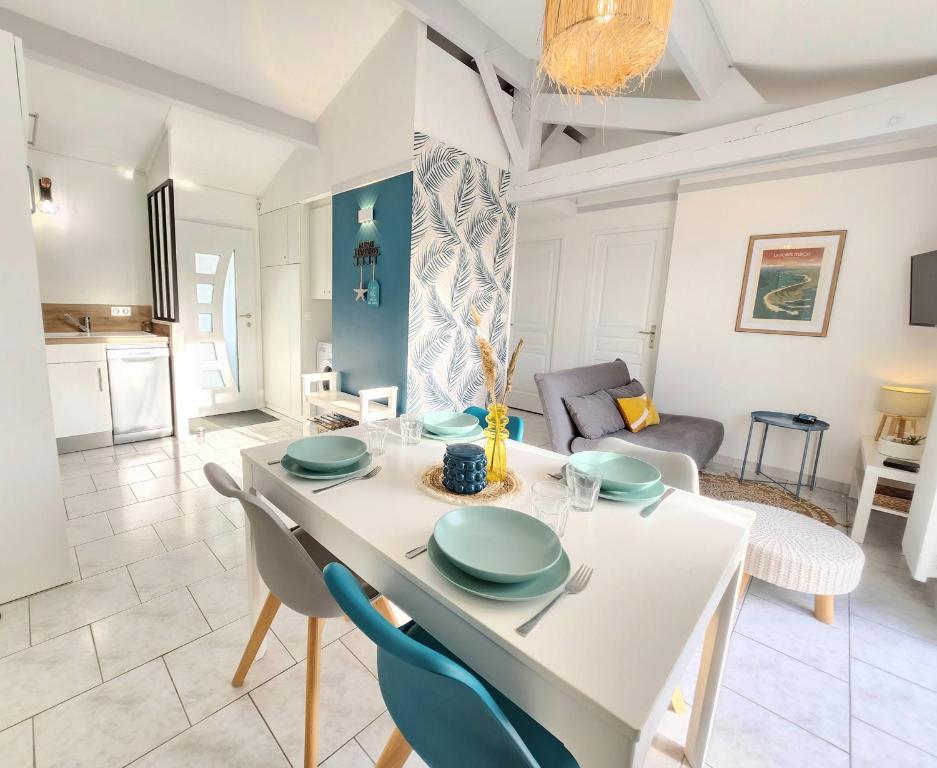 a dining room and living room with a white table and chairs at Maison Les Embruns avec piscine collective in La Faute-sur-Mer