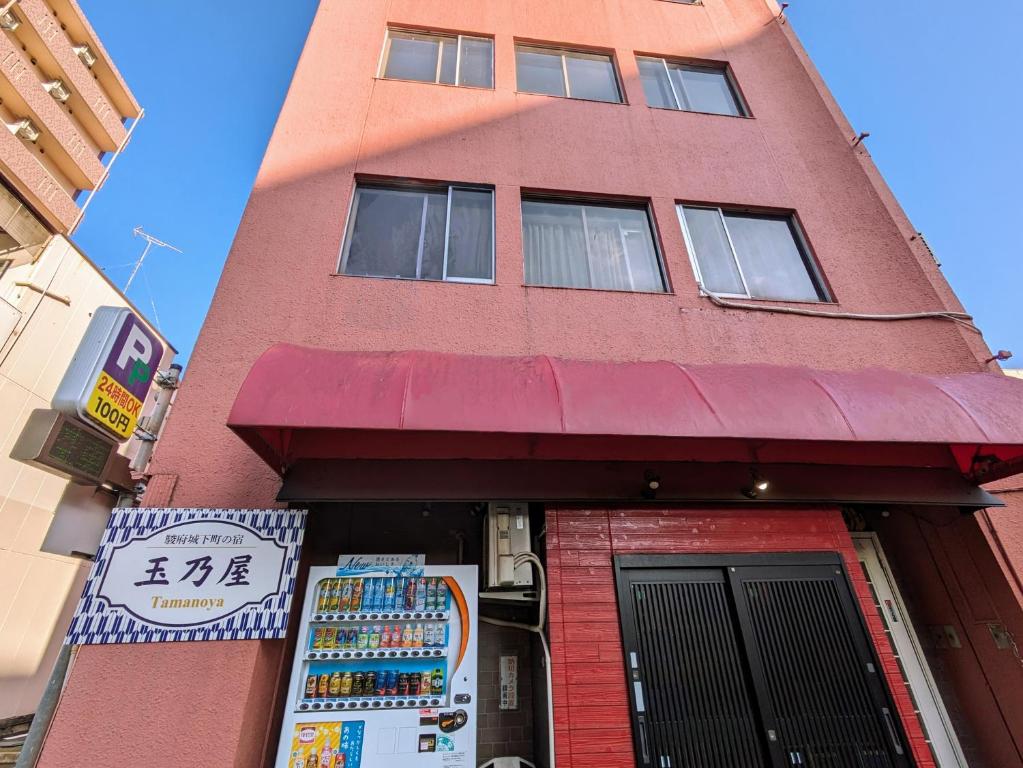 um edifício alto e vermelho com uma placa à frente. em 駿府城下町の宿　玉乃屋 em Shizuoka