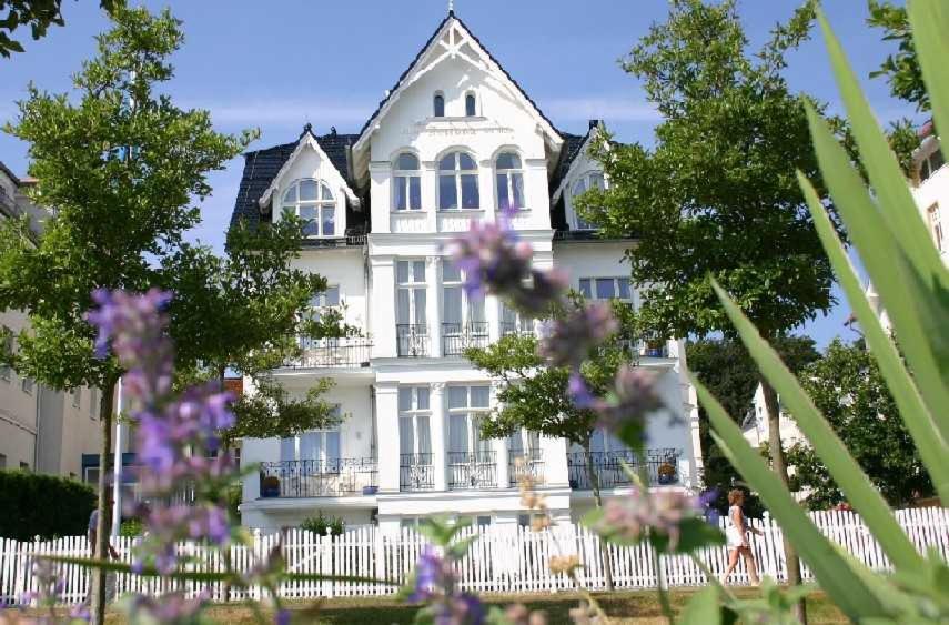 ein weißes Haus mit einem Zaun und lila Blumen in der Unterkunft Villa Fortuna mit Meerblick in Bansin in Bansin