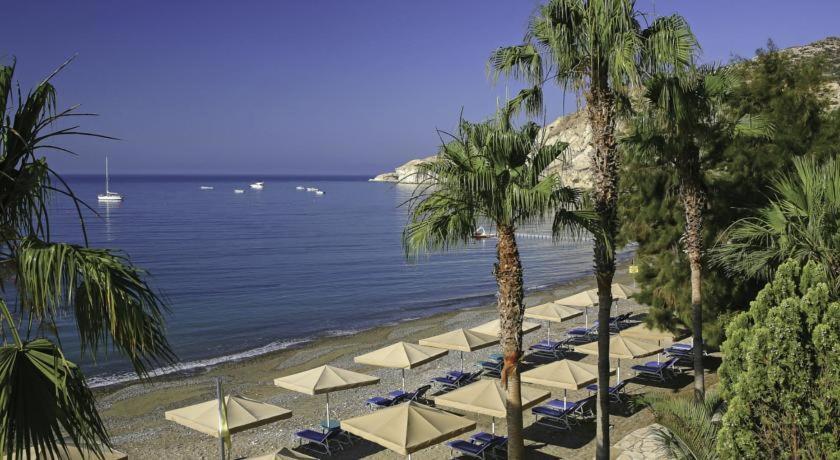 een strand met witte parasols en palmbomen en de oceaan bij Yialos Apartments in Pissouri