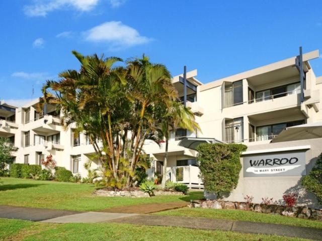 a large white building with a palm tree in front of it at Warroo Apartments in Alexandra Headland