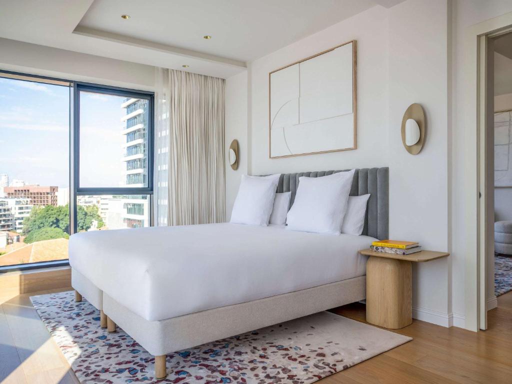 a bedroom with a white bed and a large window at Elkonin Tel Aviv - MGallery Hotel Collection in Tel Aviv