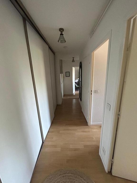 - un long couloir avec des murs blancs et du parquet dans l'établissement Appartement agréable 1 chambre, à Mérignac