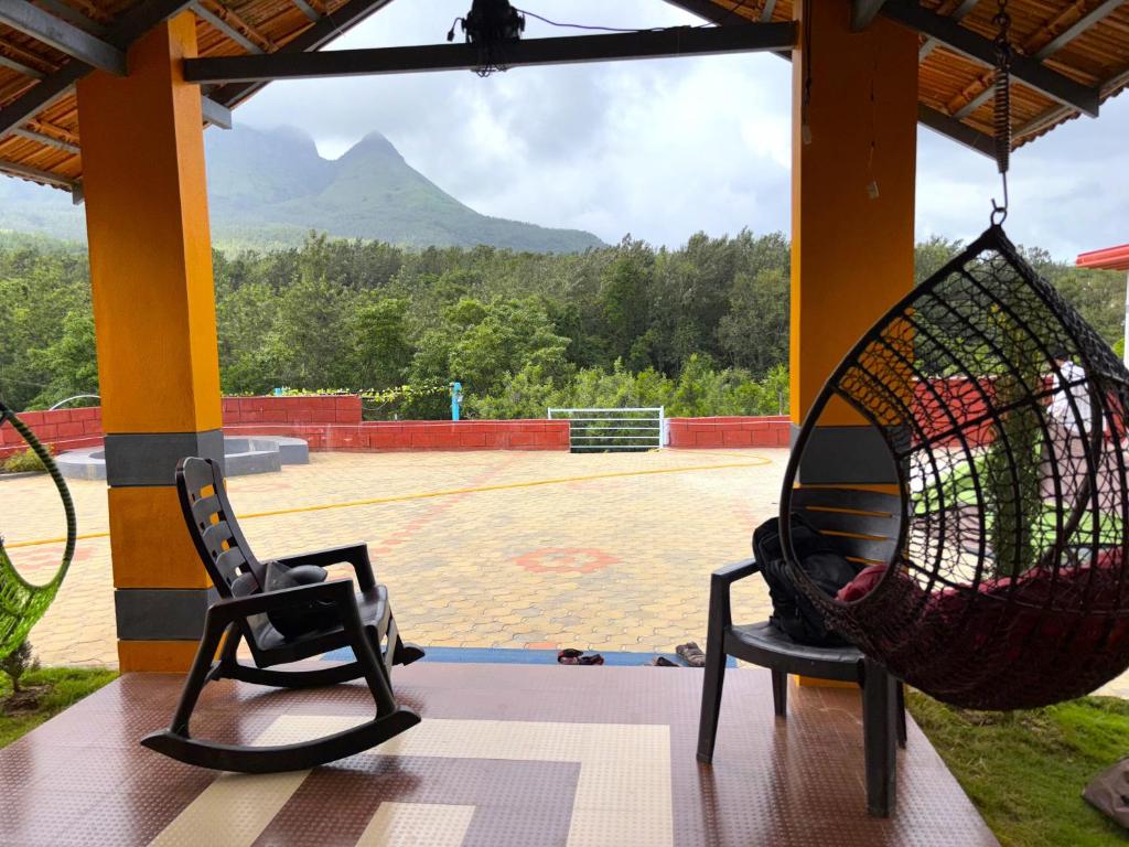 2 chaises assises sur une terrasse couverte avec un court de tennis dans l'établissement STAYMAKER Siri Vismaya Home Stay, à Chikmagalur