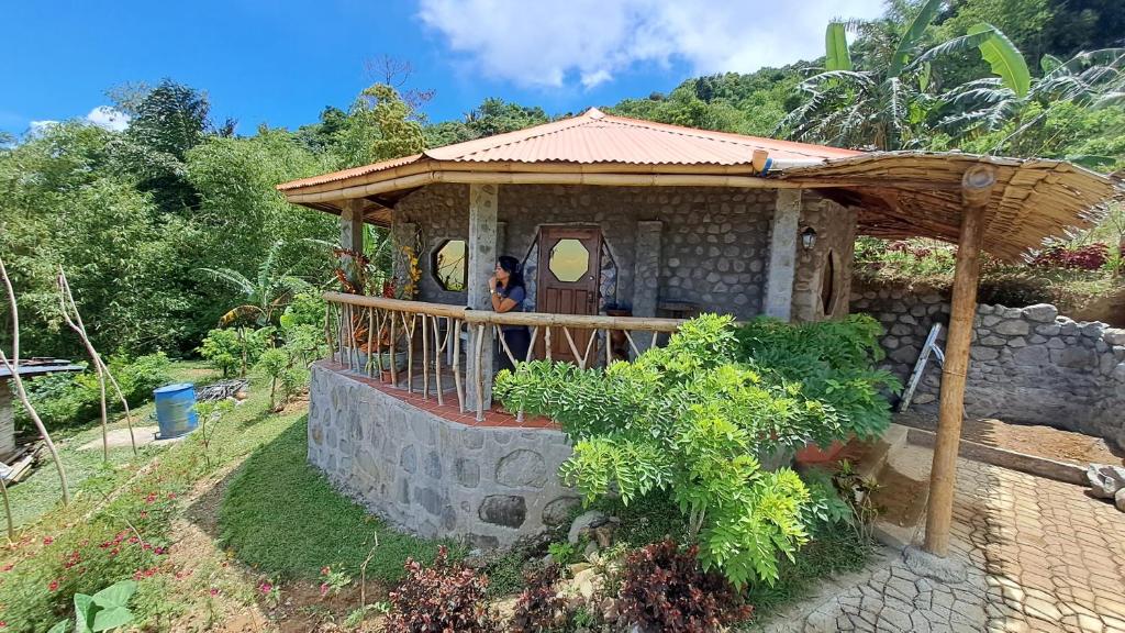 un pequeño edificio con una persona de pie en un porche en Camiguin Romantic Luxury Stonehouse on Eco-Farm at 700masl, en Mambajao